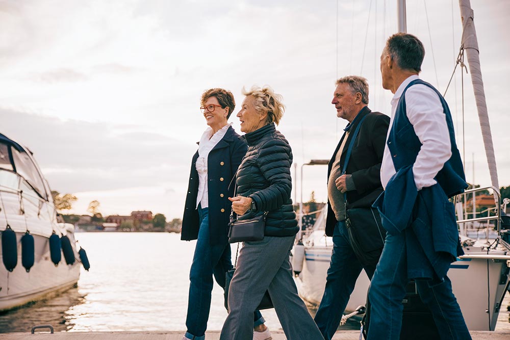 Fyra äldre vänner promenerar leende på en brygga i Stockholms hamn